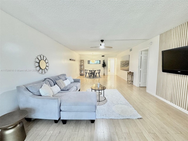 living room featuring ceiling fan, light wood-type flooring, and a textured ceiling