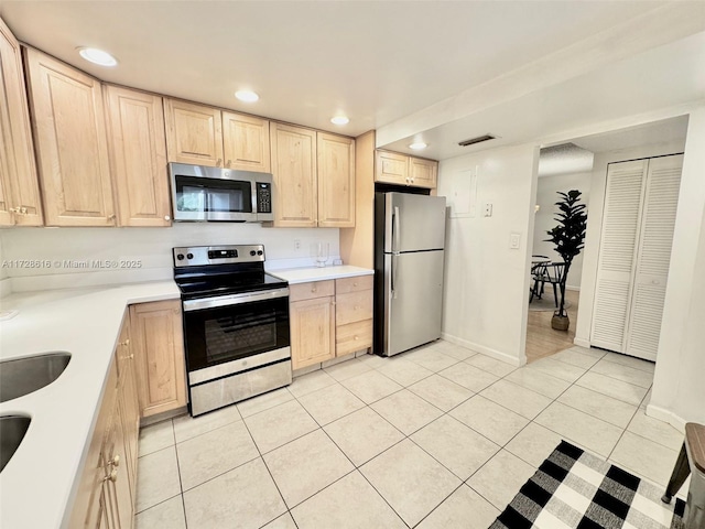 kitchen with light brown cabinetry, stainless steel appliances, and light tile patterned flooring