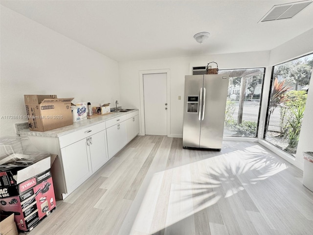 kitchen featuring light wood-type flooring, white cabinetry, stainless steel fridge, and sink