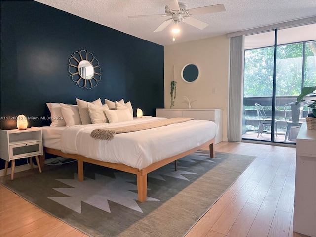 bedroom with ceiling fan, access to exterior, light hardwood / wood-style floors, a textured ceiling, and a wall of windows