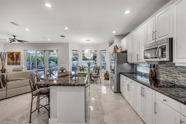 kitchen featuring white cabinetry, stainless steel appliances, tasteful backsplash, an island with sink, and decorative light fixtures