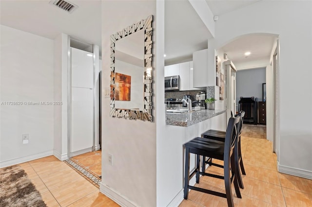 kitchen featuring light tile patterned floors, appliances with stainless steel finishes, stone counters, and white cabinetry