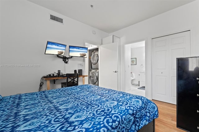 bedroom with stacked washer / dryer, ensuite bathroom, a closet, and hardwood / wood-style floors