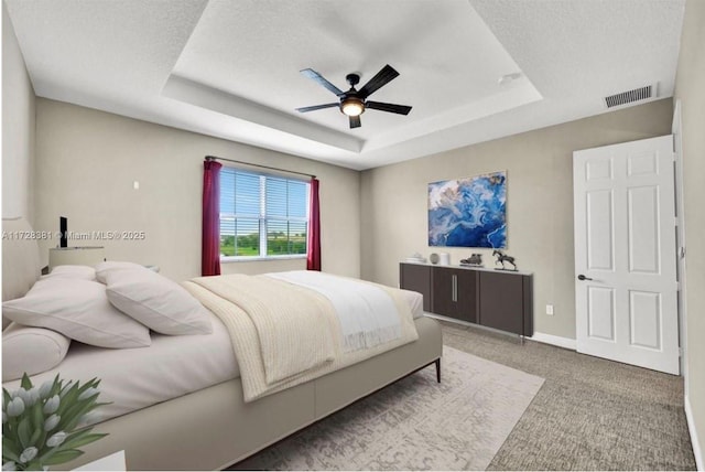 carpeted bedroom featuring a textured ceiling, ceiling fan, and a tray ceiling