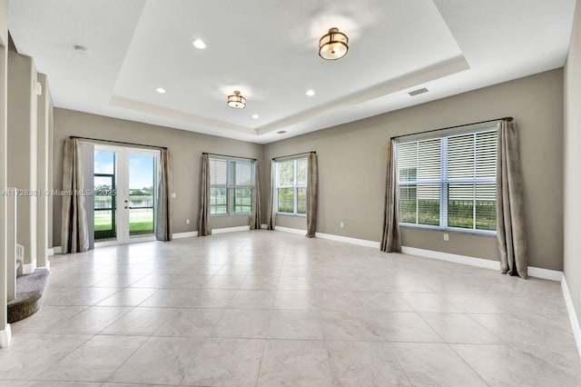 empty room with a tray ceiling and light tile patterned flooring