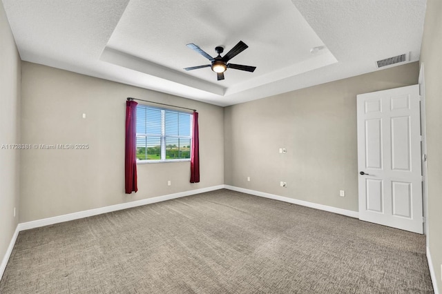 empty room with a textured ceiling, ceiling fan, carpet, and a raised ceiling