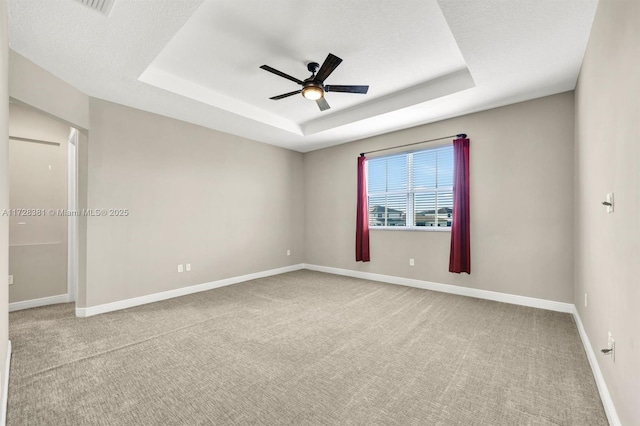 empty room with a raised ceiling, light colored carpet, ceiling fan, and a textured ceiling