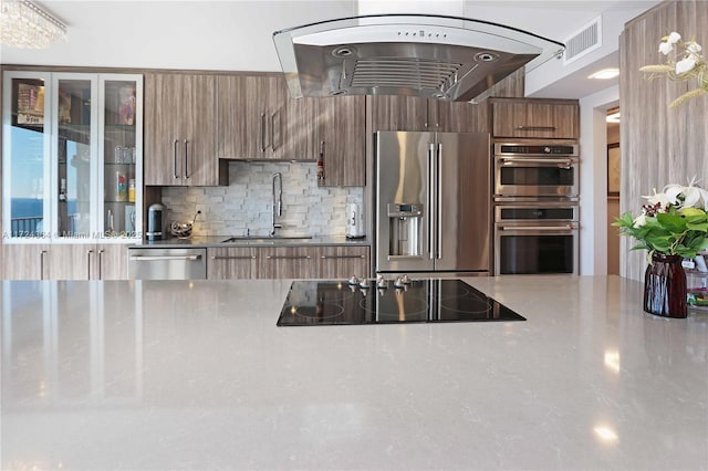 kitchen with a sink, visible vents, appliances with stainless steel finishes, backsplash, and brown cabinetry