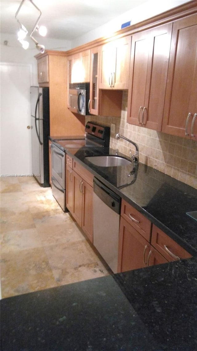 kitchen featuring appliances with stainless steel finishes, backsplash, dark stone counters, and sink