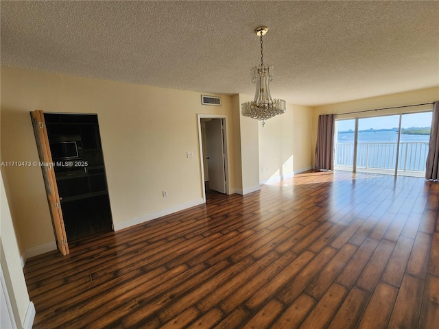 unfurnished room featuring a textured ceiling, dark hardwood / wood-style floors, a notable chandelier, and a water view