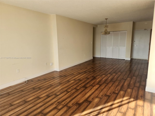 spare room with dark wood-type flooring and an inviting chandelier