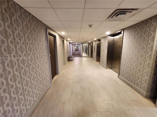 hallway featuring elevator, a paneled ceiling, and light hardwood / wood-style flooring