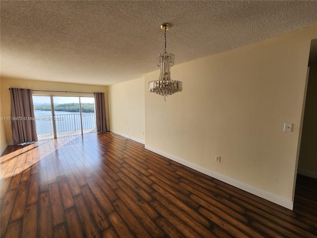 empty room featuring a textured ceiling, dark hardwood / wood-style flooring, a water view, and a chandelier