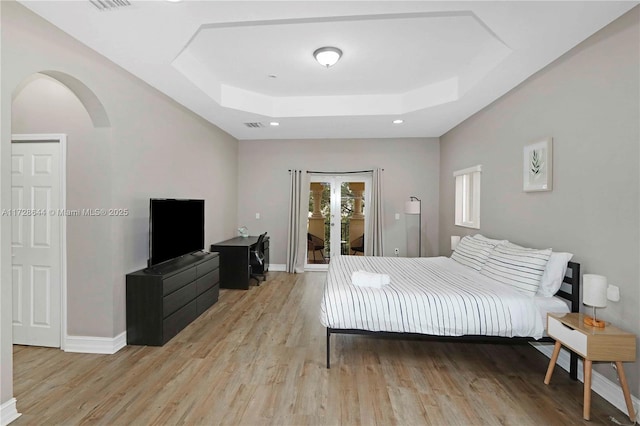 bedroom with a tray ceiling, access to outside, and light wood-type flooring