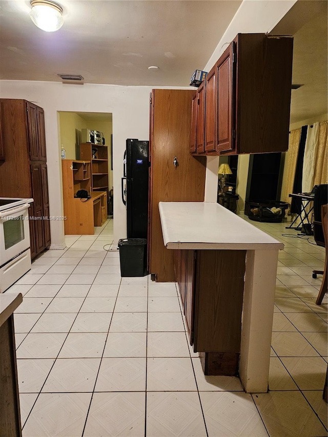 kitchen with black refrigerator, white electric range, kitchen peninsula, and light tile patterned flooring