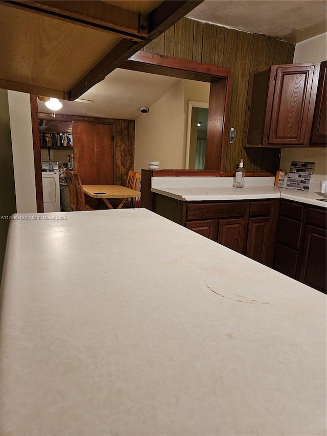 kitchen featuring dark brown cabinetry, beam ceiling, wooden walls, and independent washer and dryer