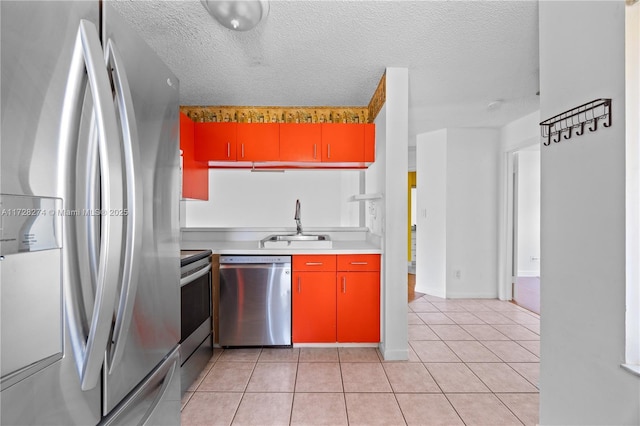 kitchen with a textured ceiling, light tile patterned floors, appliances with stainless steel finishes, and sink