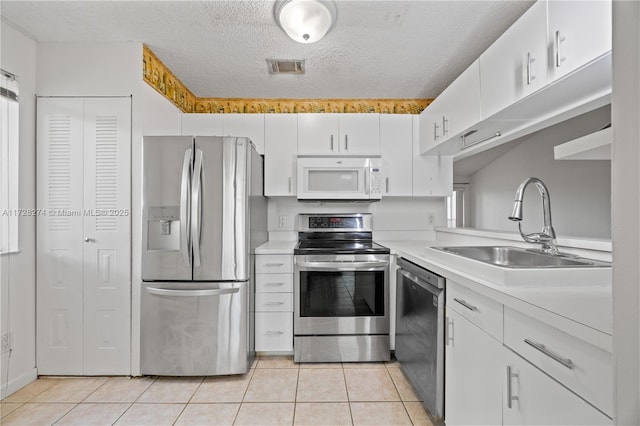 kitchen featuring appliances with stainless steel finishes, white cabinetry, sink, light tile patterned floors, and a textured ceiling