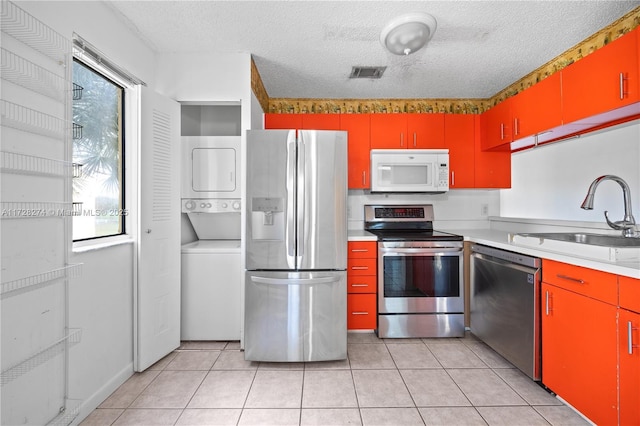 kitchen featuring stacked washer and dryer, sink, stainless steel appliances, and a textured ceiling