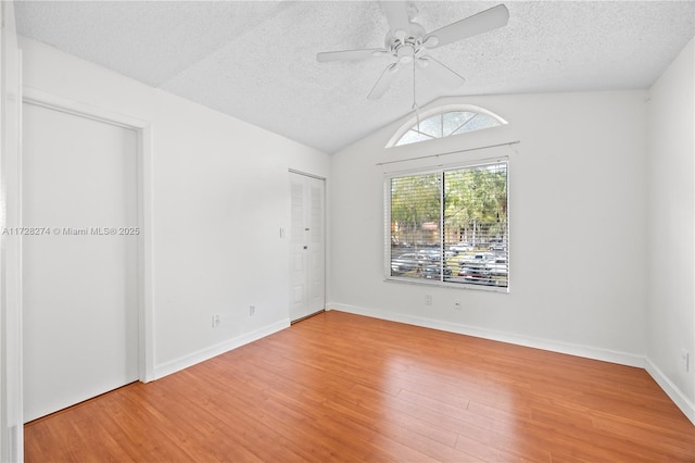 spare room with a textured ceiling, ceiling fan, lofted ceiling, and wood-type flooring