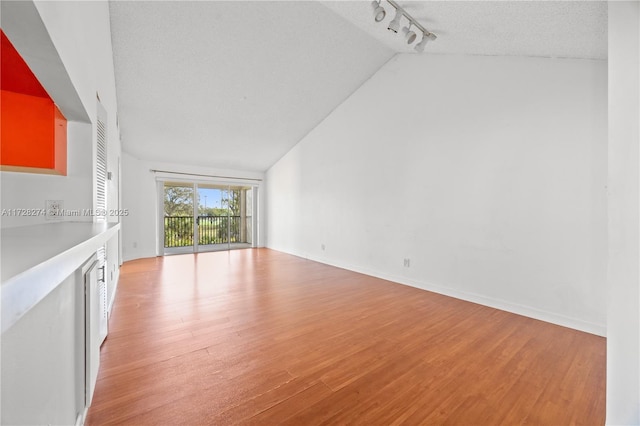 unfurnished living room with rail lighting, a textured ceiling, light hardwood / wood-style flooring, and vaulted ceiling