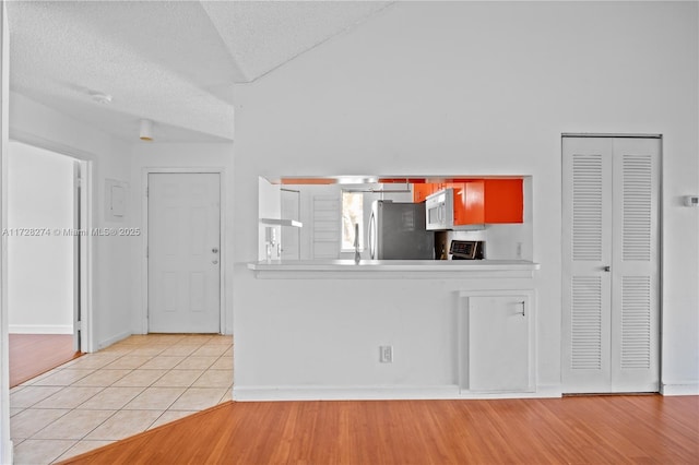 kitchen with a textured ceiling, light tile patterned floors, lofted ceiling, and stainless steel refrigerator