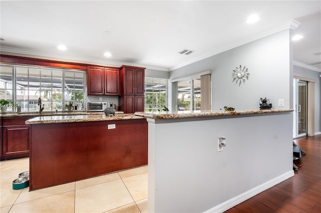 kitchen with light stone counters, light tile patterned floors, ornamental molding, and a kitchen island