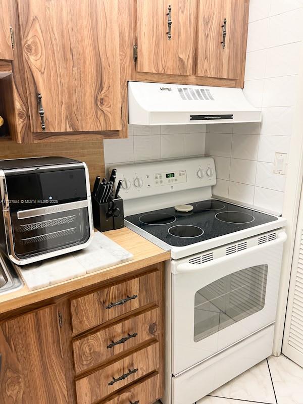 kitchen featuring electric range, light tile patterned floors, and tasteful backsplash