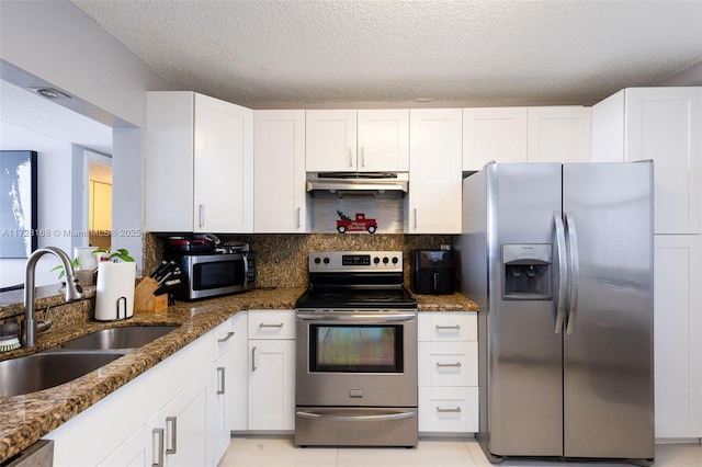 kitchen with appliances with stainless steel finishes, white cabinets, dark stone counters, and sink