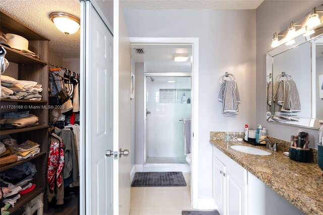 bathroom with a textured ceiling, tile patterned floors, walk in shower, and vanity