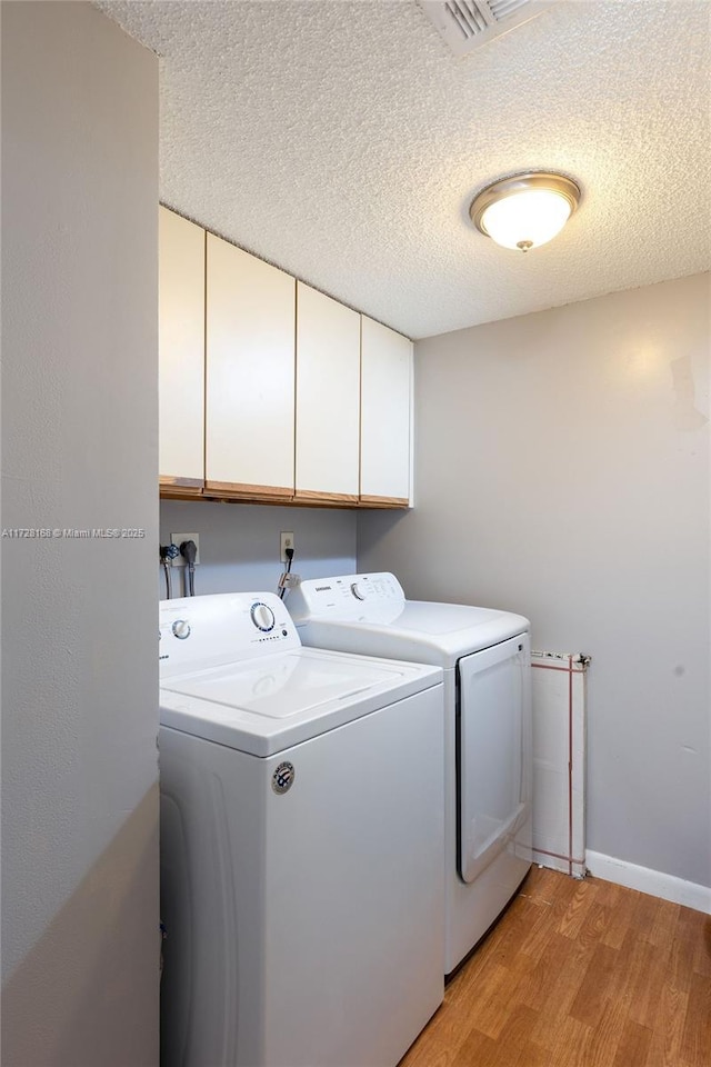 laundry area featuring a textured ceiling, cabinets, washer and clothes dryer, and light hardwood / wood-style flooring