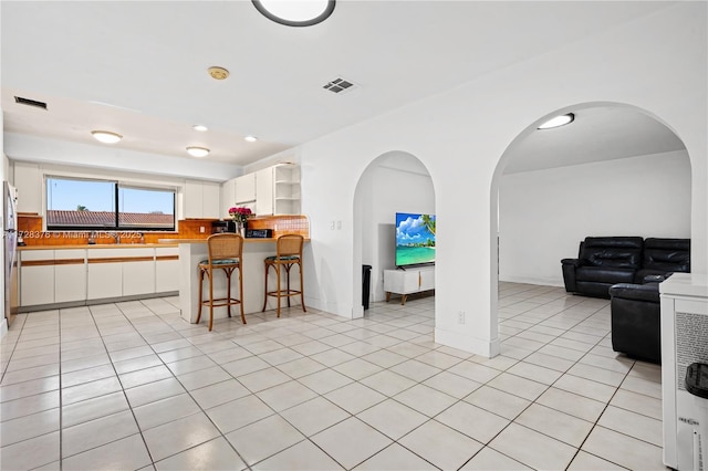 kitchen with backsplash, kitchen peninsula, light tile patterned floors, a kitchen breakfast bar, and white cabinets