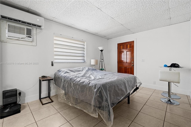 bedroom featuring a paneled ceiling, light tile patterned flooring, and a wall mounted air conditioner