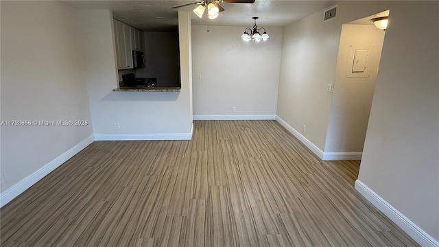 spare room featuring light wood-type flooring and ceiling fan with notable chandelier