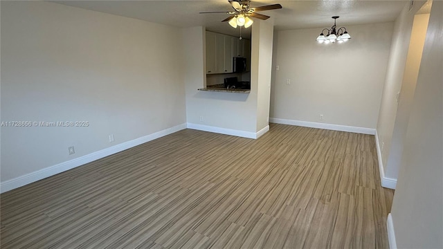 unfurnished living room with light wood-type flooring and ceiling fan with notable chandelier