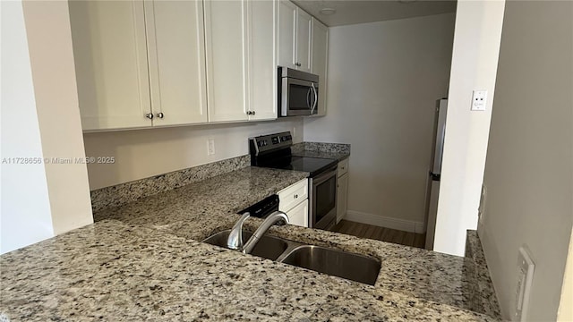 kitchen with light stone countertops, white cabinets, stainless steel appliances, sink, and kitchen peninsula