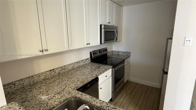 kitchen featuring hardwood / wood-style floors, stainless steel appliances, white cabinets, and light stone counters