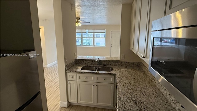 kitchen with a textured ceiling, white cabinetry, sink, stone countertops, and light hardwood / wood-style flooring