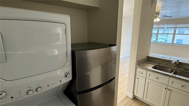 kitchen with a textured ceiling, white cabinetry, stacked washer / drying machine, sink, and stone counters