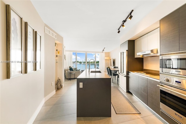 kitchen featuring a center island with sink, sink, appliances with stainless steel finishes, a water view, and rail lighting