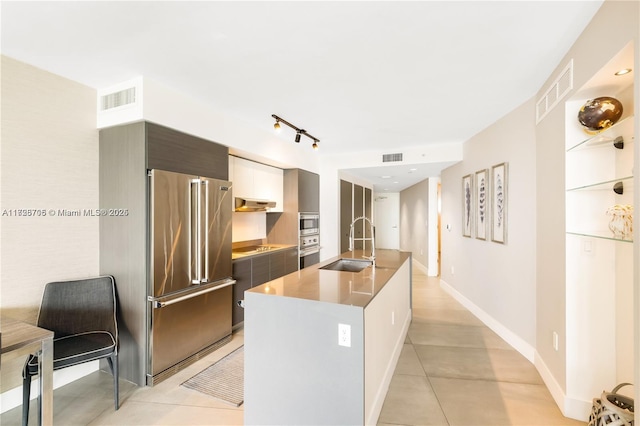 kitchen with sink, dark brown cabinetry, high end fridge, an island with sink, and black electric cooktop