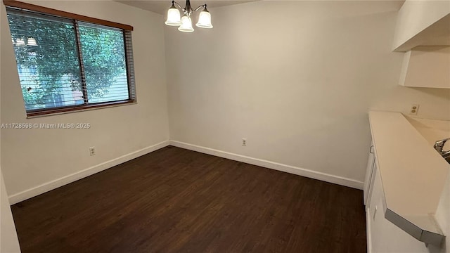 spare room with dark hardwood / wood-style flooring and an inviting chandelier