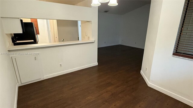 interior space with black fridge, kitchen peninsula, dark hardwood / wood-style flooring, and white cabinets