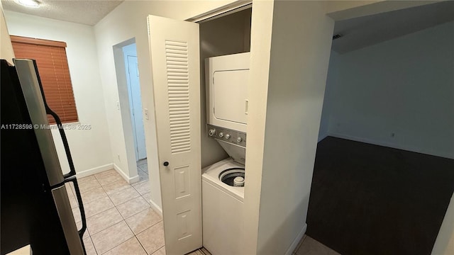 clothes washing area featuring stacked washer / dryer, light tile patterned floors, and a textured ceiling