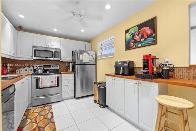 kitchen featuring ceiling fan, tasteful backsplash, light tile patterned floors, stainless steel appliances, and white cabinets