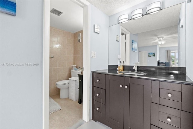 bathroom with toilet, vanity, tile walls, ceiling fan, and a textured ceiling