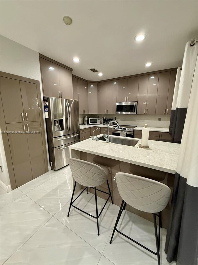 kitchen with sink, a breakfast bar area, appliances with stainless steel finishes, light stone counters, and kitchen peninsula