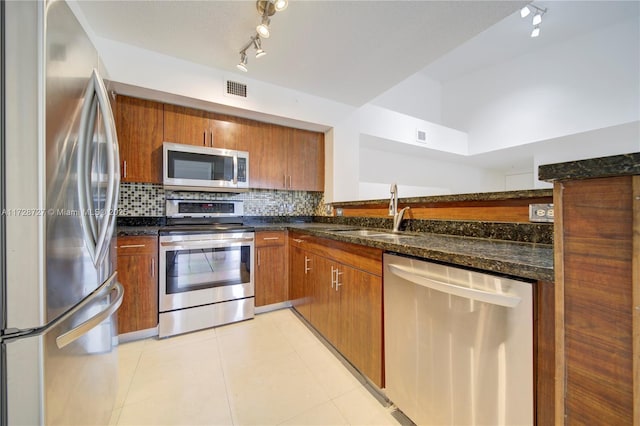 kitchen featuring backsplash, dark stone countertops, sink, light tile patterned flooring, and stainless steel appliances