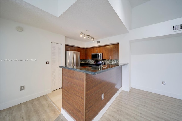 kitchen featuring backsplash, kitchen peninsula, light wood-type flooring, stainless steel appliances, and a textured ceiling