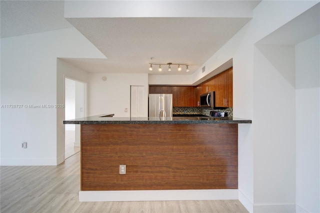 kitchen with backsplash, light hardwood / wood-style floors, kitchen peninsula, stainless steel appliances, and dark stone counters